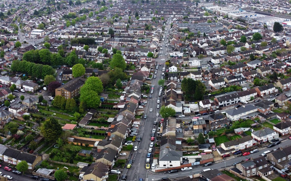 An aerial view of a residential neighbourhood in Rush Green, Romford, showing a mixture of detached and terraced houses with driveways, gardens, and parked cars lining the streets. The image reveals a