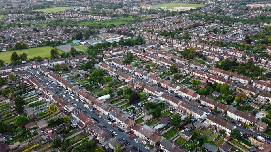 An aerial view of a residential neighbourhood in Rush Green, Romford, showing a mixture of detached and terraced houses with driveways, gardens, and parked cars lining the streets. The image reveals a
